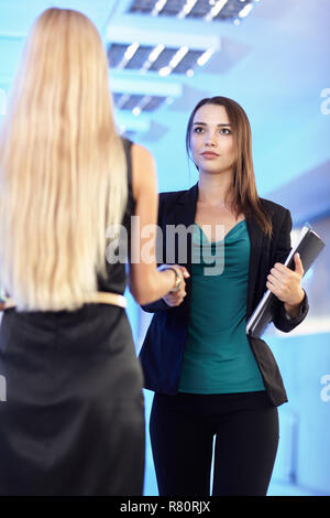 Due ragazze in ufficio con le cartelle con le carte in mano. Giovani donne agitare le mani. Blue sala vuota sullo sfondo Foto Stock