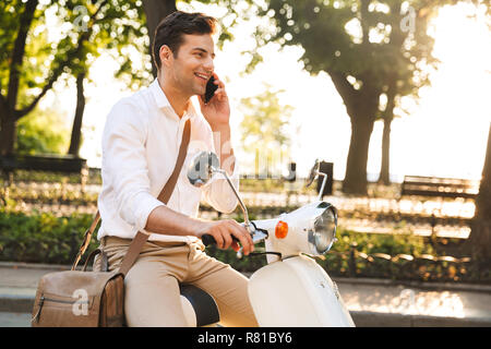 Immagine di un bel giovane uomo d affari passeggiate all'aperto su scooter parla al telefono cellulare. Foto Stock