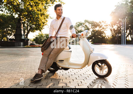 Felice giovane imprenditore seduto su una moto all'aperto che guarda lontano Foto Stock