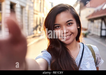 Giovane donna asiatica sorridente e tenendo selfies nella città Foto Stock