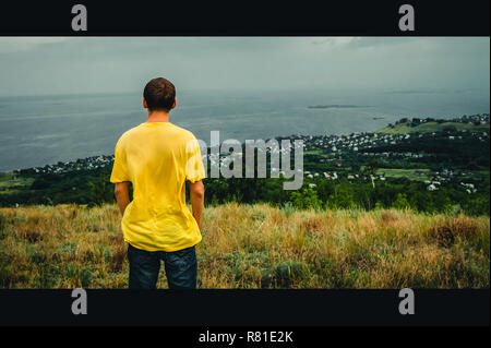 Un giovane uomo sta con la sua schiena contro lo sfondo del villaggio. Questo mondo ha bisogno di un nuovo eroe. Lo stile del cinema Foto Stock