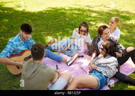 Amici a suonare la chitarra al picnic nel parco di estate Foto Stock