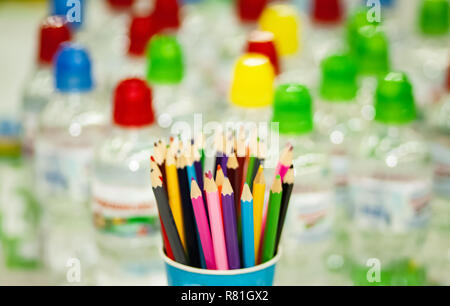 Vetro con matite colorate. Un sacco di bottiglie di acqua sullo sfondo. Foto Stock