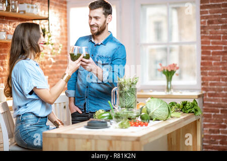 Coppia giovane di vegetariani bere frullato fresco su la cucina con il verde il cibo sano a casa Foto Stock