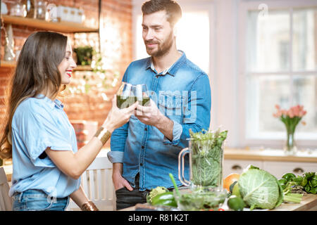 Coppia giovane di vegetariani bere frullato fresco su la cucina con il verde il cibo sano a casa Foto Stock