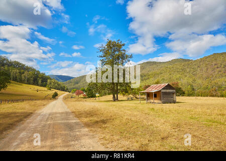 Un entroterra australiano di scena nel Nuovo Galles del Sud con una strada che corre attraverso la campagna e un vecchio stagno homestead circondata da montagne Foto Stock