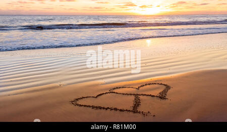 Il giorno di San Valentino di sunny beach. Due cuori attirato in sabbia, concetto di amore Foto Stock