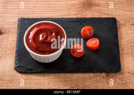 Ketchup salsa nella ciotola e pomodori sul tavolo di legno. Foto Stock