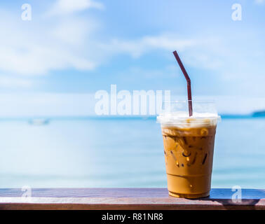 Tè freddo con il latte o il tradizionale tè tailandese in plastica trasparente in vetro con paglia sulla barra di legno sul cielo blu e seascape sfondo sulla giornata del sole con co Foto Stock