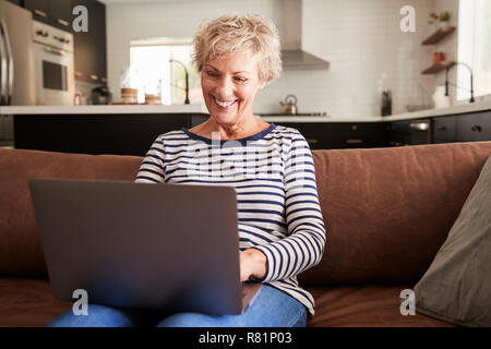 Senior white donna seduta sul lettino usando il computer portatile Foto Stock