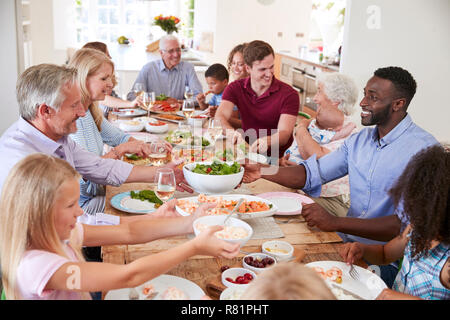 Gruppo di Multi-Generation la famiglia e gli amici seduti attorno al tavolo e godendo di pasto Foto Stock