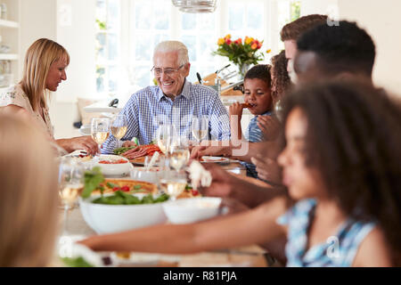 Gruppo di Multi-Generation la famiglia e gli amici seduti attorno al tavolo e godendo di pasto Foto Stock