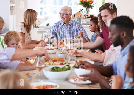 Gruppo di Multi-Generation la famiglia e gli amici seduti attorno al tavolo e godendo di pasto Foto Stock