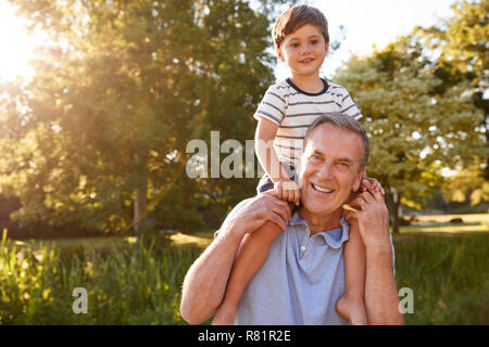Ritratto di Nonno dando nipote Ride su spalle in estate Park Foto Stock