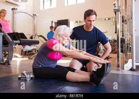 Senior donna esercizio in palestra essendo incoraggiati da Personal Trainer Foto Stock