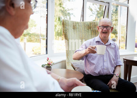 Maschi e femmine residenti in seduta sedie e parlando in casa di riposo Foto Stock