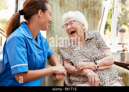 Senior donna seduta in poltrona e ridere con infermiere in casa di riposo Foto Stock