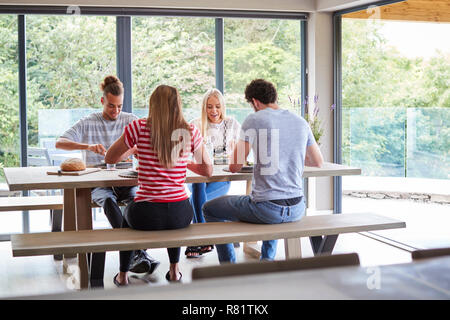Multi etnico gruppo di quattro giovani amici adulti a mangiare una cena informale delle parti in una moderna sala da pranzo Foto Stock