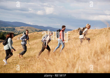 Multi gruppo etnico di felice giovani amici adulti in salita durante una escursione in montagna, vista laterale Foto Stock