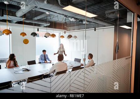 Imprenditrice dando presentazione nella sala consiliare visto attraverso la Sala Riunioni finestra Foto Stock