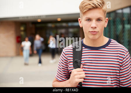 Ritratto del maschio serio studente di scuola superiore al di fuori del college edificio con altri studenti di adolescenti in background Foto Stock