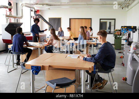 Classe di alta scuola gli studenti seduti a banchi di lavoro ascolto di insegnante nel design e tecnologia lezione Foto Stock