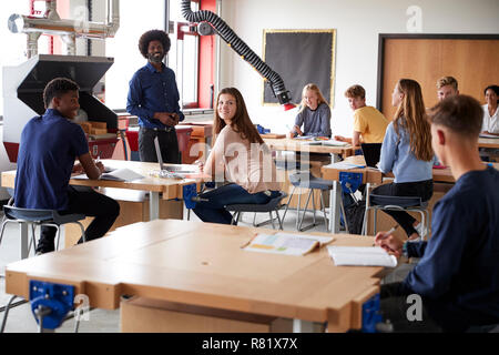 Classe di alta scuola gli studenti seduti a banchi di lavoro ascolto di insegnante nel design e tecnologia lezione Foto Stock