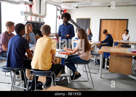 Un gruppo di studenti di scuola superiore seduta a banchi di lavoro ascolto di insegnante nel design e tecnologia lezione Foto Stock