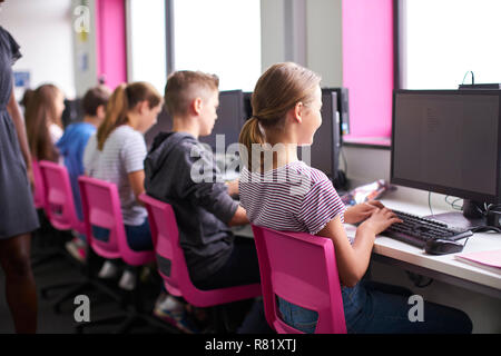 Vista posteriore del Maestro femmina di supervisione di linea di alta scuola gli studenti lavorano a schermate in Classe Computer Foto Stock