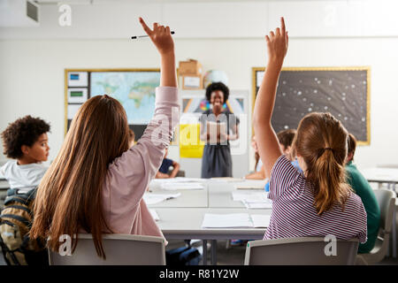 Gli studenti delle scuole superiori alzando le mani per rispondere alla domanda impostata dall insegnante in classe Foto Stock