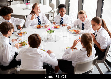 Un gruppo di studenti di scuola superiore che indossano uniformi di sedersi a tavola e mangiare il pranzo nella caffetteria Foto Stock