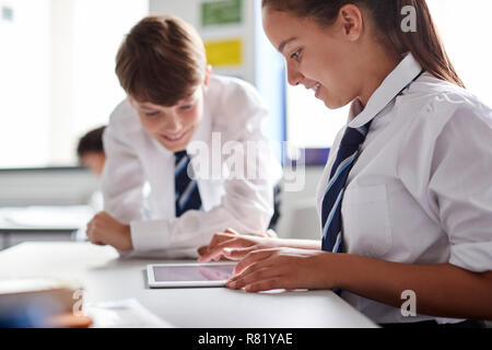 Due studenti di scuola superiore che indossano uniformi di lavorare insieme al Desk utilizzando tavoletta digitale Foto Stock
