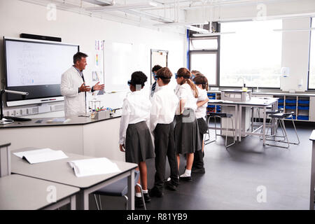 Maschio della High School Tutor insegnamento di alta scuola gli studenti indossano uniformi nella Classe di Scienze Foto Stock