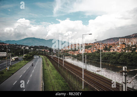 Autostrada, fiume e ferrovia nel lussureggiante città collinare di Medellín, in Colombia, con il rosso delle case di barrios costruita sulle colline Foto Stock