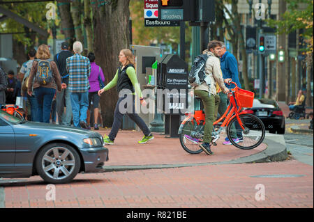 Portland, Oregon, Stati Uniti d'America - 8 Ottobre 2016: un uomo su un arancio Portland noleggio biciclette è in attesa di attraversare un centro di crocevia dove le auto, i pedoni una Foto Stock