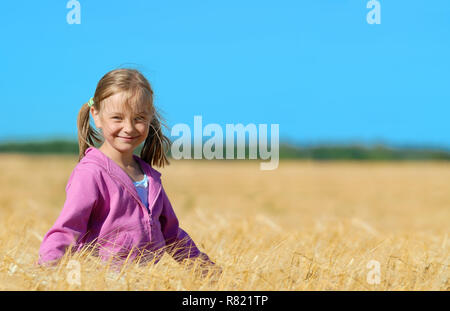 Poco carino ragazza bionda sul campo di grano Foto Stock