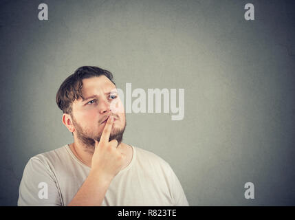 Adulto Uomo chunky toccando le labbra con il dito e guarda lontano in pensieri profondi rendendo la decisione Foto Stock