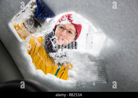 Giovane donna la pulizia di una vettura di ghiaccio e neve Foto Stock