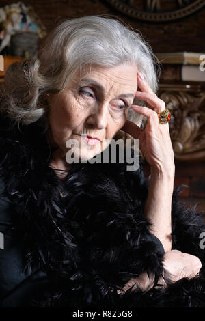 Ritratto di triste donna senior in boa che pongono a casa Foto Stock