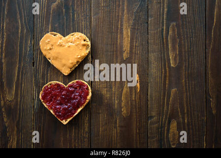 A forma di cuore ad panini con burro di arachidi e gelatina su sfondo di legno Foto Stock