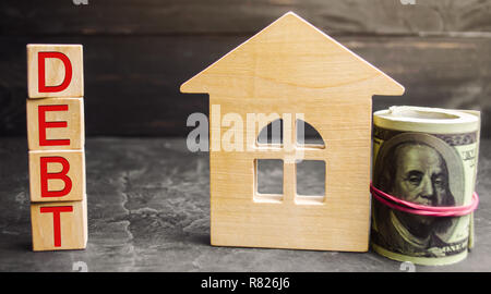 Miniatura casa in legno, dollari e l'iscrizione ' ' del debito. Settore immobiliare, casa di risparmio, prestiti il concetto di mercato. Il pagamento della tassa immobiliare. Ipoteca. R Foto Stock