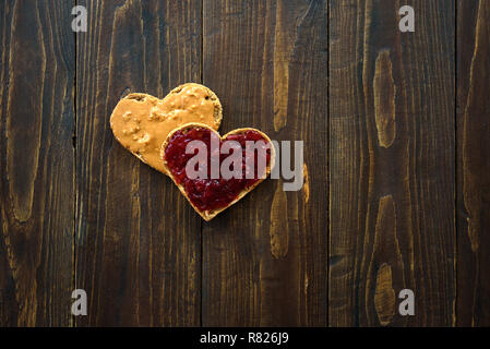 A forma di cuore ad panini con burro di arachidi e gelatina su sfondo di legno Foto Stock