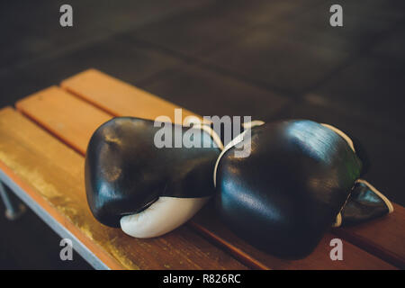 Due nero guantoni da pugilato giacciono su pugilato ring in bianco. L'ombra dell'anello cade sui pavimenti. Foto Stock