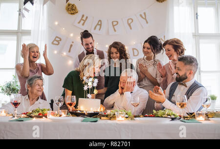 Un uomo anziano con famiglia multigenerazionali festeggia il compleanno sulla parte interna. Foto Stock