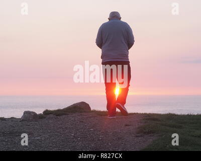 Uomo anziano incorniciata dal tramonto vista posteriore Foto Stock