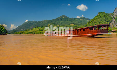 Un lungo tour marrone vele di imbarcazioni verso il basso il possente fiume Mekong in Laos con le lussureggianti montagne verdi fodera riva Foto Stock