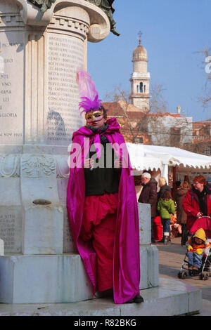 Una giovane ragazza di carnevale abiti fantasiosi e maschera pone da una statua in Campo Santa Margherita, Dorsoduro, Venezia, Italia Foto Stock