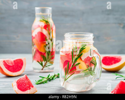 Infusa detox acqua con succo di pompelmo e rosmarino in mason jar e bottiglia di vetro grigio su un tavolo di legno. dieta mangiare sano e perdita di peso concetto, copia spazio per il testo Foto Stock