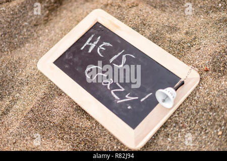 Lavagna con un preavviso: egli è pazzo! Mettere sulla spiaggia Foto Stock