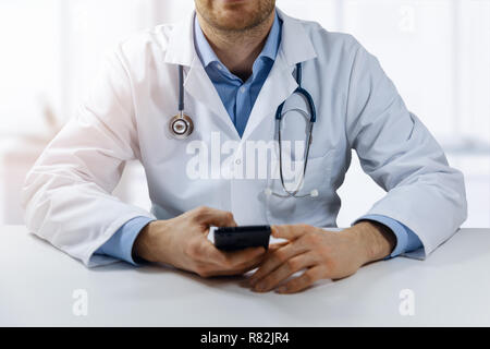 Online di consultazione medica - medico seduti a tavola in ufficio e utilizzando smart phone Foto Stock